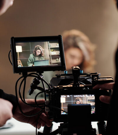 Close-up of steadicam screens with female model using laptop by table